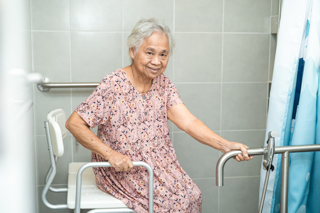 Elderly woman using a medical shower chair and handrail.
